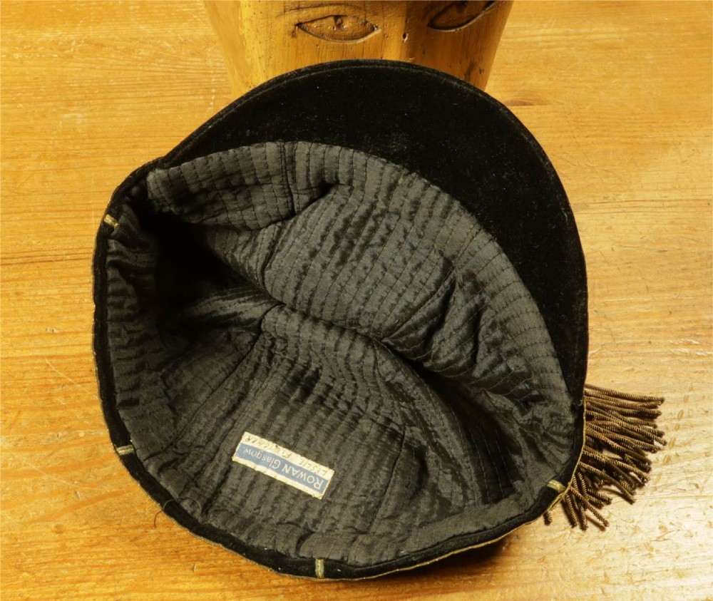 A 1920s black velvet sports cap featuring metallic braid piping, embroidered dates, monogram crest, and a prominent hanging tassel. View XII