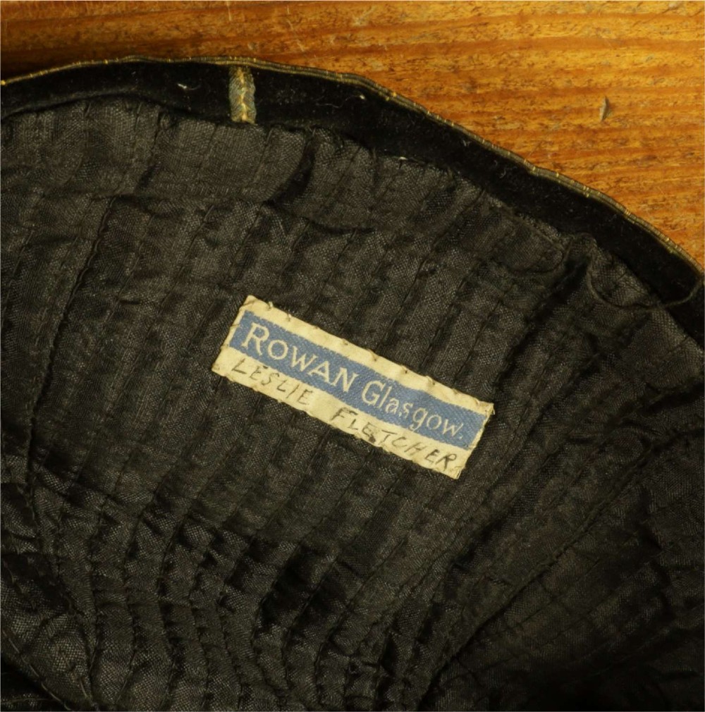 A 1920s black velvet sports cap featuring metallic braid piping, embroidered dates, monogram crest, and a prominent hanging tassel. View XIII