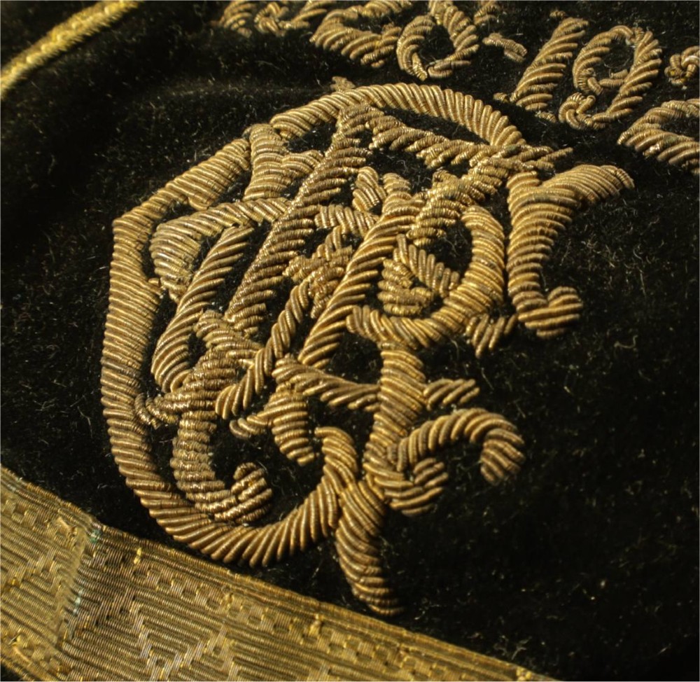 A 1920s black velvet sports cap featuring metallic braid piping, embroidered dates, monogram crest, and a prominent hanging tassel. View XV