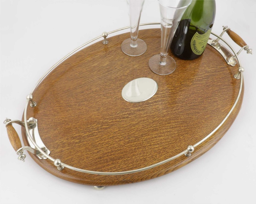 An oval polished oak tray featuring a silver-plated raised gallery rail, twin wooden-handled side grips, ball feet, and an unengraved central silver oval medallion. View II