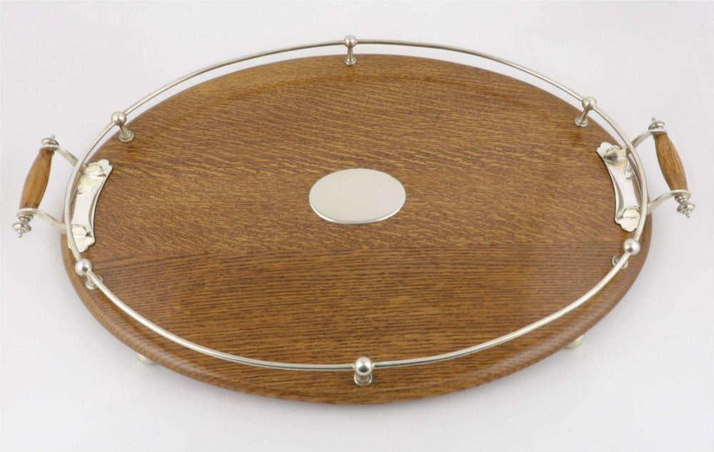 An oval polished oak tray featuring a silver-plated raised gallery rail, twin wooden-handled side grips, ball feet, and an unengraved central silver oval medallion. View III