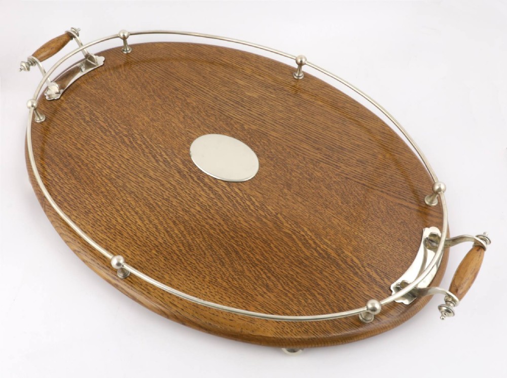 An oval polished oak tray featuring a silver-plated raised gallery rail, twin wooden-handled side grips, ball feet, and an unengraved central silver oval medallion. View IV