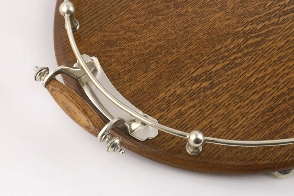 An oval polished oak tray featuring a silver-plated raised gallery rail, twin wooden-handled side grips, ball feet, and an unengraved central silver oval medallion. View V