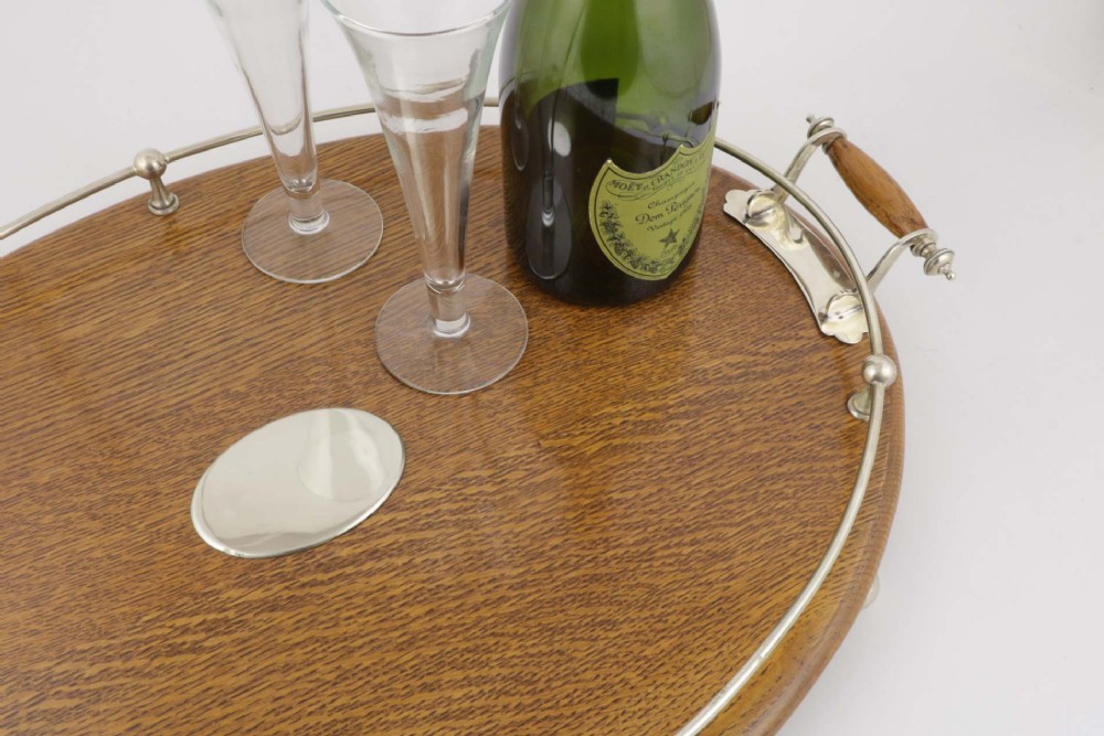 An oval polished oak tray featuring a silver-plated raised gallery rail, twin wooden-handled side grips, ball feet, and an unengraved central silver oval medallion. View VI