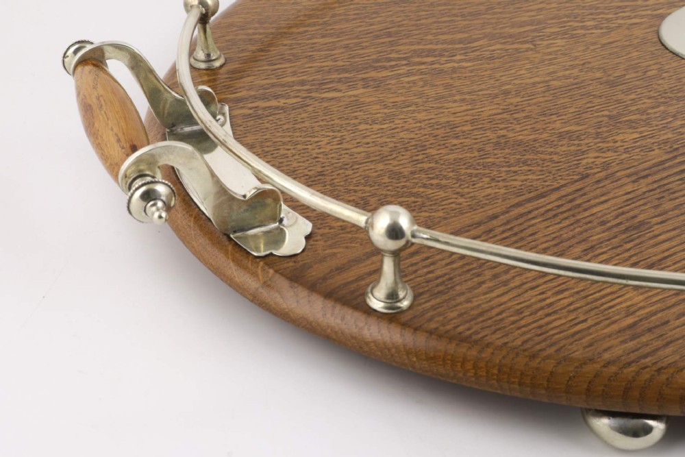 An oval polished oak tray featuring a silver-plated raised gallery rail, twin wooden-handled side grips, ball feet, and an unengraved central silver oval medallion. View VII