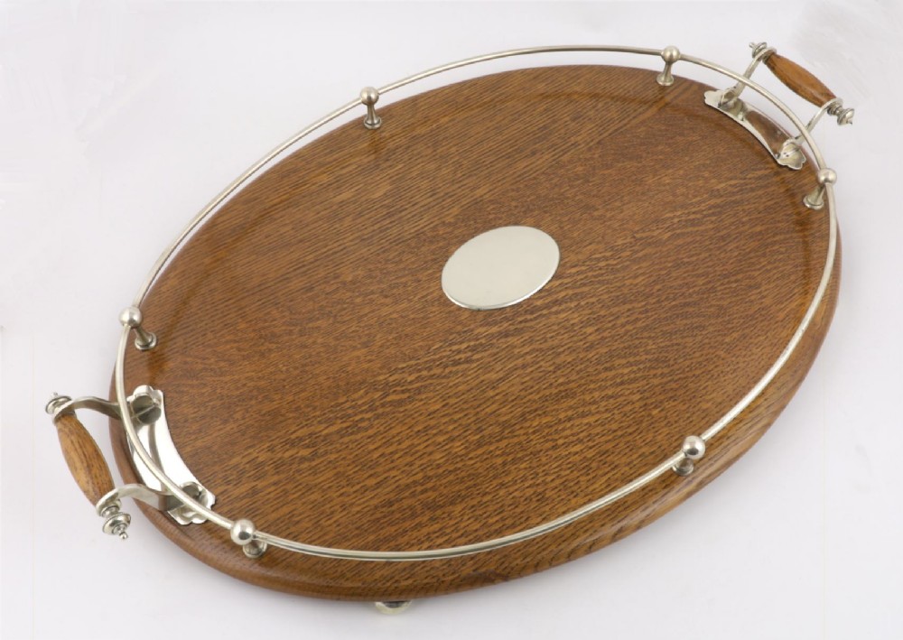 An oval polished oak tray featuring a silver-plated raised gallery rail, twin wooden-handled side grips, ball feet, and an unengraved central silver oval medallion. View VIII