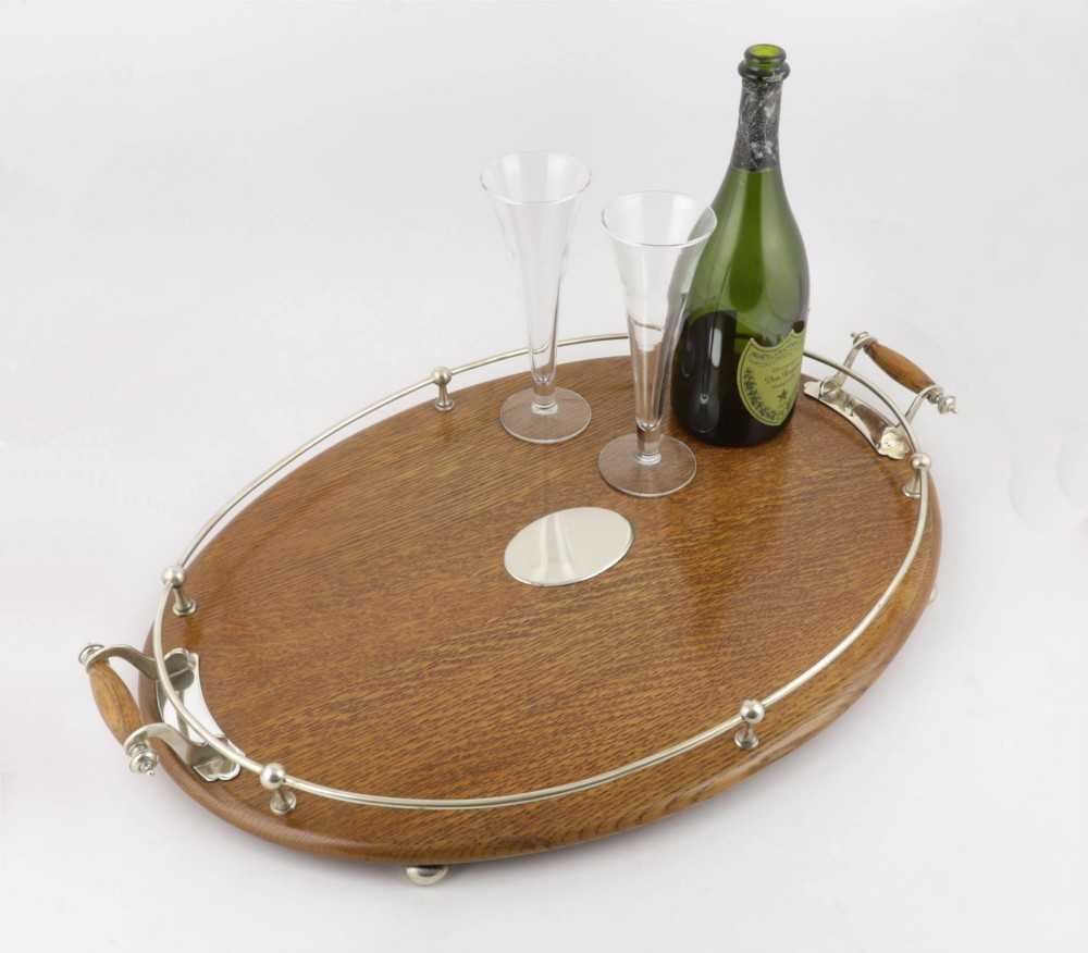 An oval polished oak tray featuring a silver-plated raised gallery rail, twin wooden-handled side grips, ball feet, and an unengraved central silver oval medallion. View IX