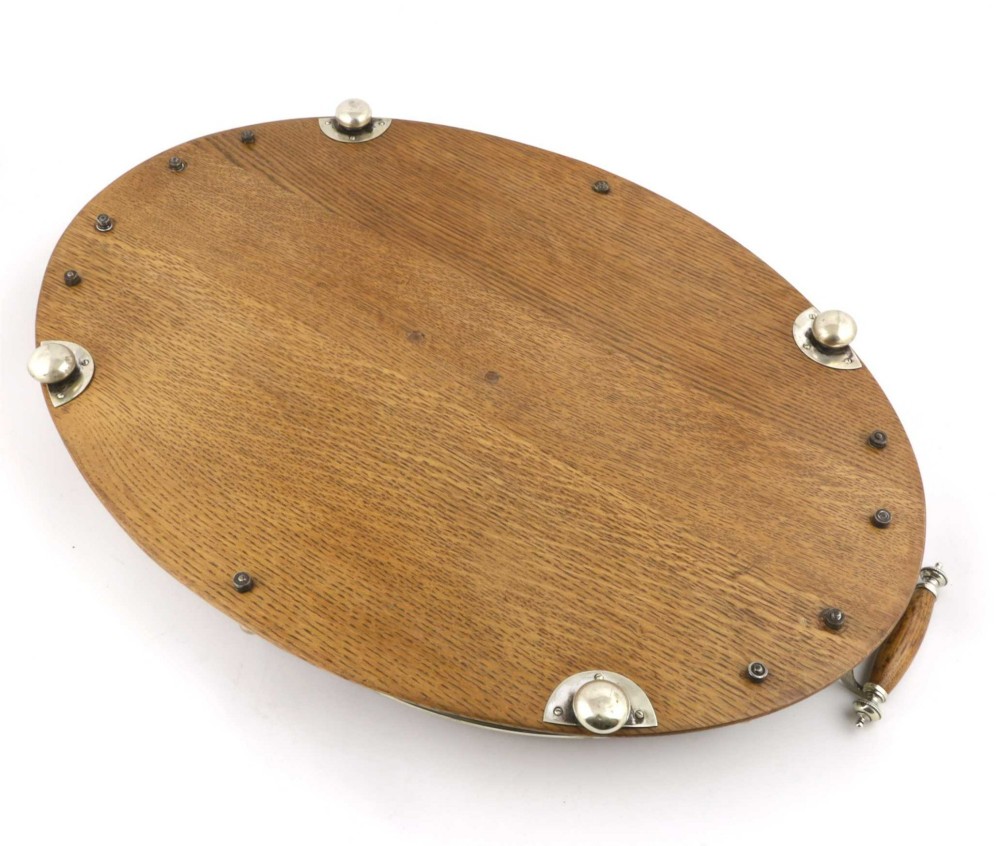 An oval polished oak tray featuring a silver-plated raised gallery rail, twin wooden-handled side grips, ball feet, and an unengraved central silver oval medallion. View X