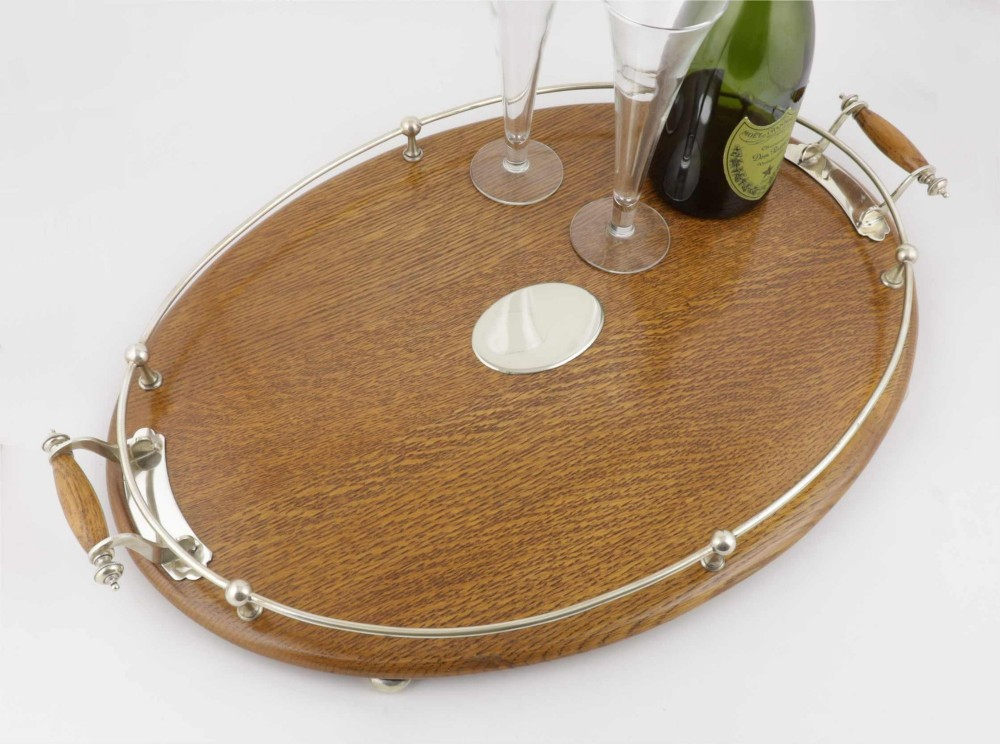 An oval polished oak tray featuring a silver-plated raised gallery rail, twin wooden-handled side grips, ball feet, and an unengraved central silver oval medallion. View XI