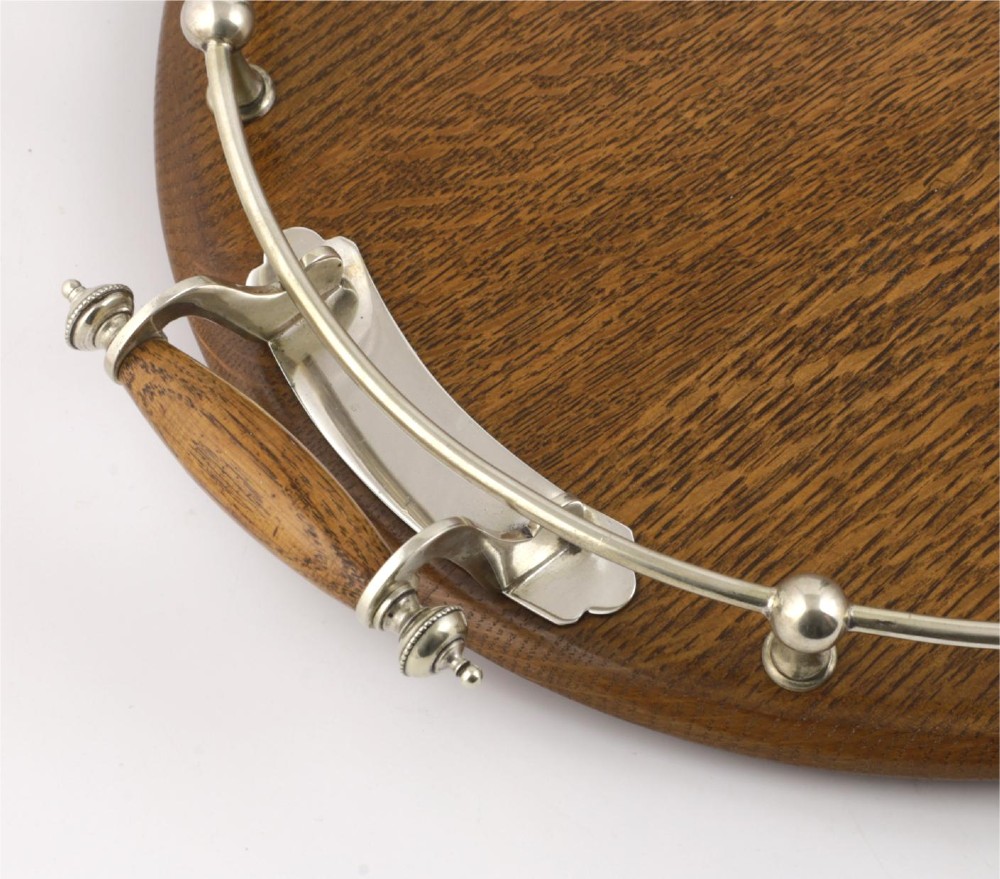 An oval polished oak tray featuring a silver-plated raised gallery rail, twin wooden-handled side grips, ball feet, and an unengraved central silver oval medallion. View XII