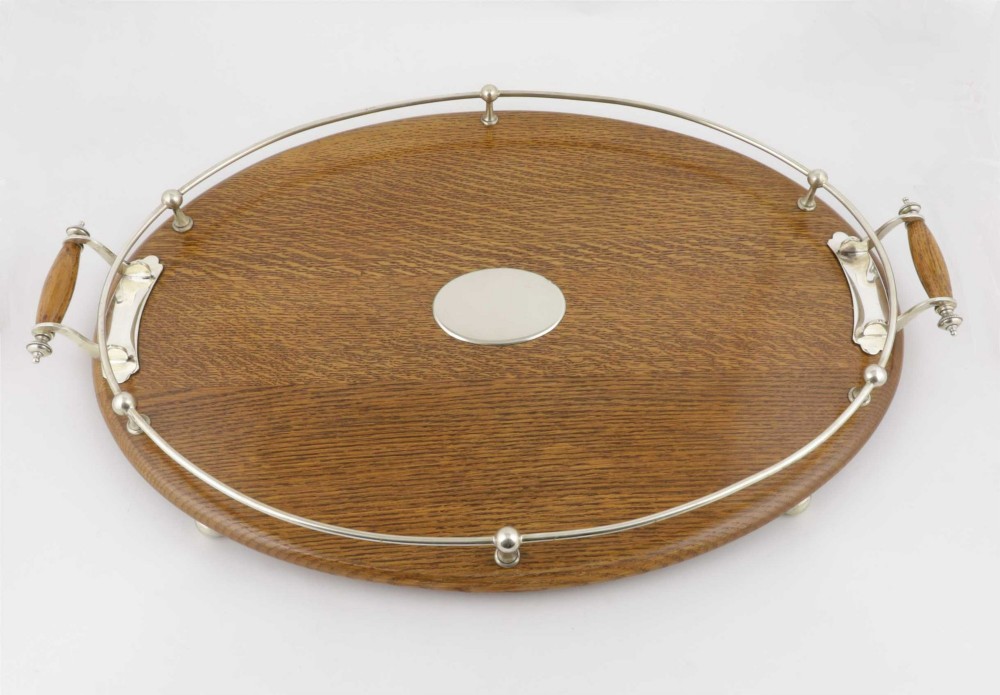 An oval polished oak tray featuring a silver-plated raised gallery rail, twin wooden-handled side grips, ball feet, and an unengraved central silver oval medallion. View XIII