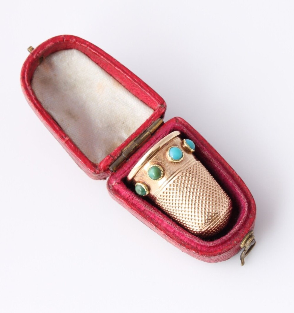 An antique Victorian 15ct gold thimble with turquoise cabochon studs displayed inside an open red leather velvet-lined case.
