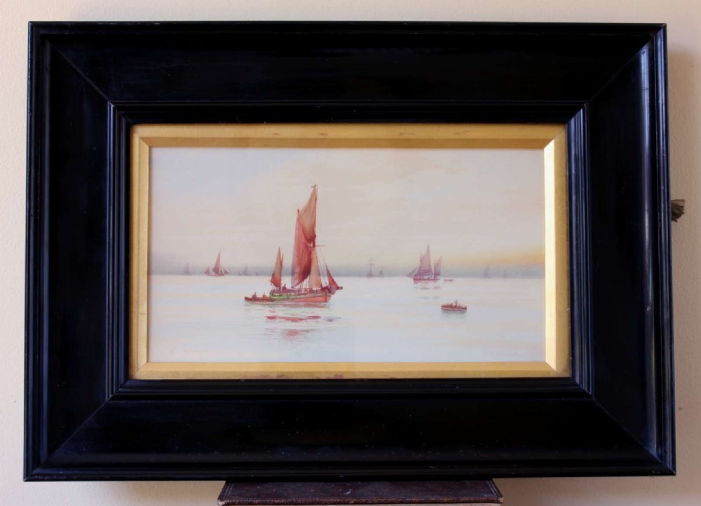 A framed early twentieth-century watercolour painting featuring red-sailed fishing boats on calm waters off Scarborough, enclosed in a thick black frame with a gold inner slip.