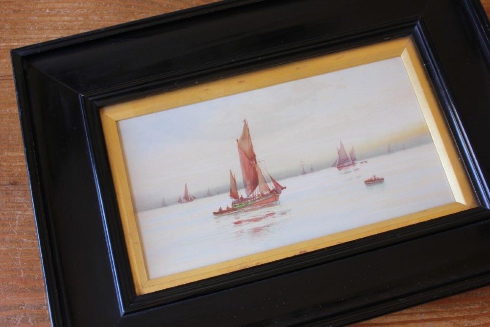 A framed early twentieth-century watercolour painting featuring red-sailed fishing boats on calm waters off Scarborough, enclosed in a thick black frame with a gold inner slip. View IX