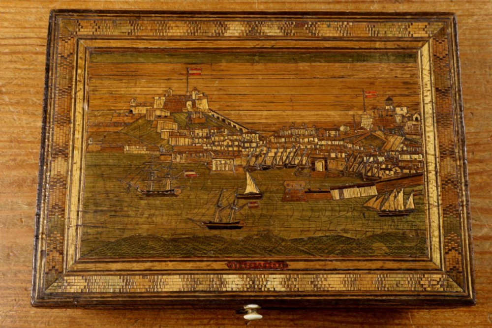 A rectangular wooden box top featuring intricate straw marquetry depicting a harbour landscape with ships, fortresses, and geometric borders.