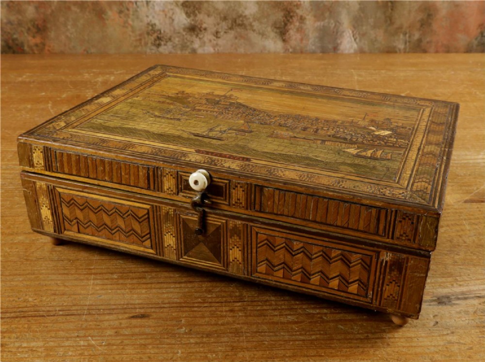 A rectangular wooden box top featuring intricate straw marquetry depicting a harbour landscape with ships, fortresses, and geometric borders. View IX