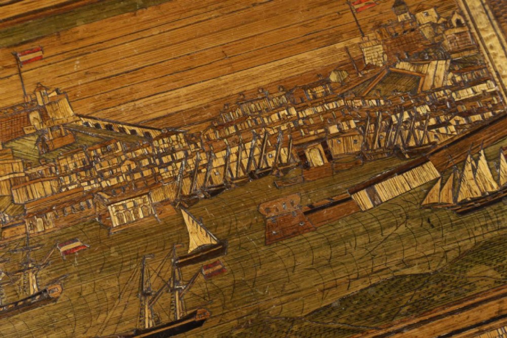 A rectangular wooden box top featuring intricate straw marquetry depicting a harbour landscape with ships, fortresses, and geometric borders. View X