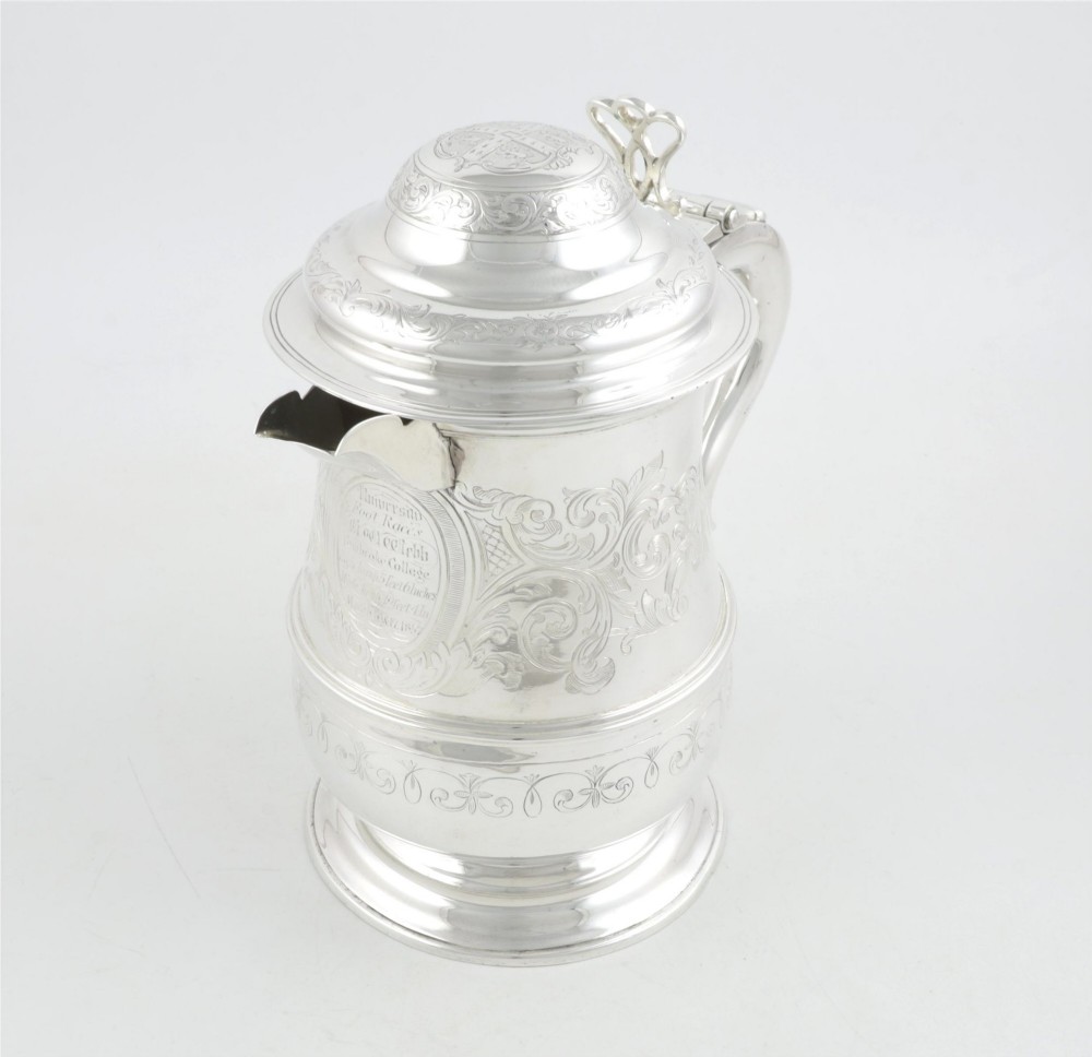 An engraved silver lidded jug featuring a hinged cap, scrolling handle, and foliate engraving across the body. View V