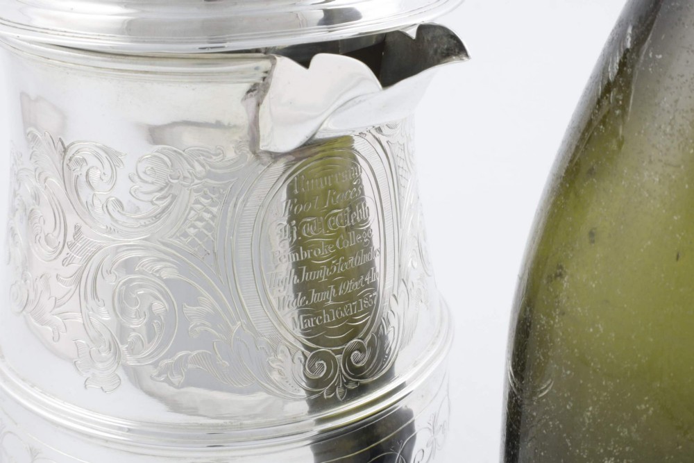 An engraved silver lidded jug featuring a hinged cap, scrolling handle, and foliate engraving across the body. View VII