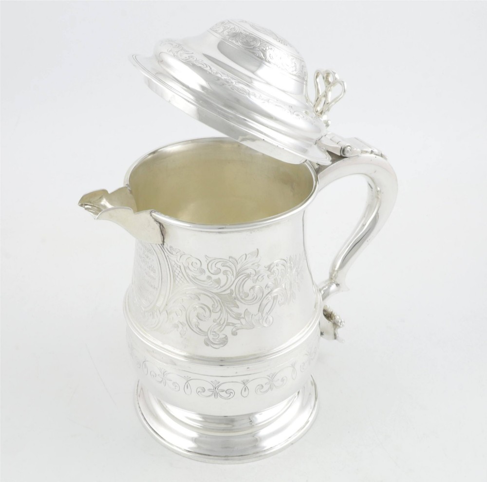 An engraved silver lidded jug featuring a hinged cap, scrolling handle, and foliate engraving across the body. View IX