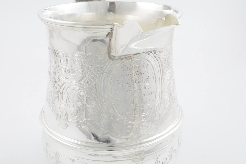An engraved silver lidded jug featuring a hinged cap, scrolling handle, and foliate engraving across the body. View X