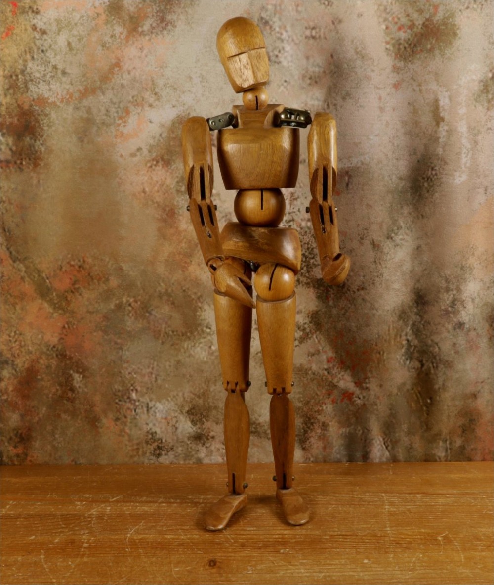 A carved teak articulated artist lay figure standing on a surface with both arms raised at the elbow joints. View III