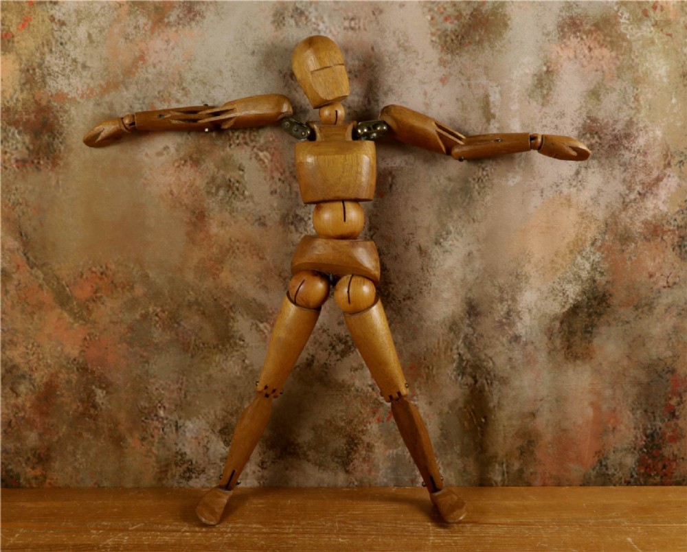 A carved teak articulated artist lay figure standing on a surface with both arms raised at the elbow joints. View V