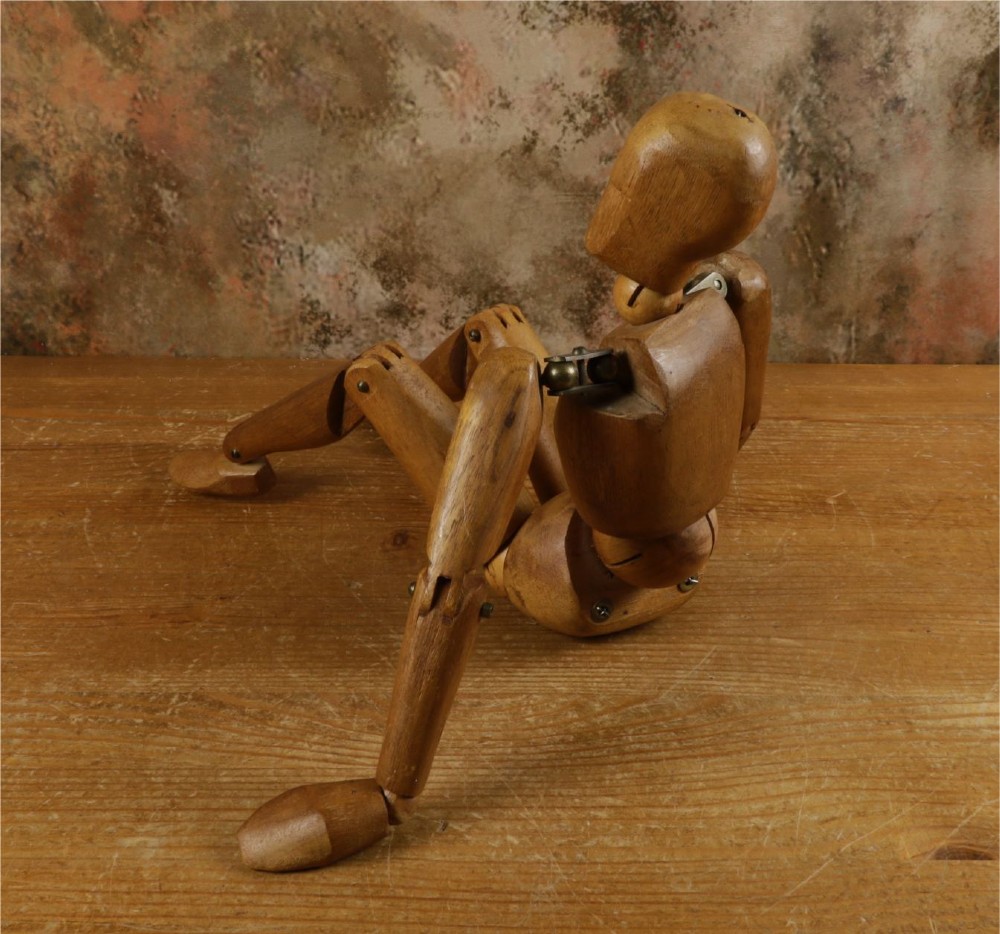 A carved teak articulated artist lay figure standing on a surface with both arms raised at the elbow joints. View IX