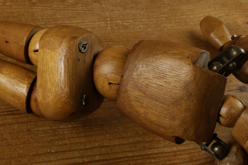 A carved teak articulated artist lay figure standing on a surface with both arms raised at the elbow joints. View XIII