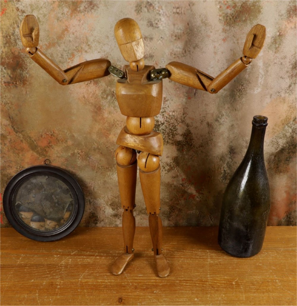 A carved teak articulated artist lay figure standing on a surface with both arms raised at the elbow joints. View XIV