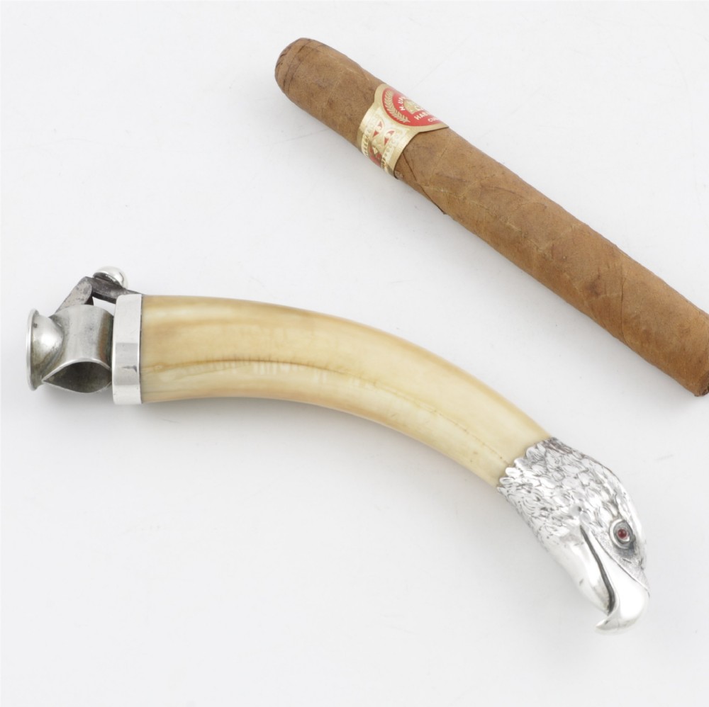 An antique cigar cutter crafted from a curved cream-coloured boar tusk fitted with a cast silver eagle head terminal and a silver cutting mechanism at the opposing end.