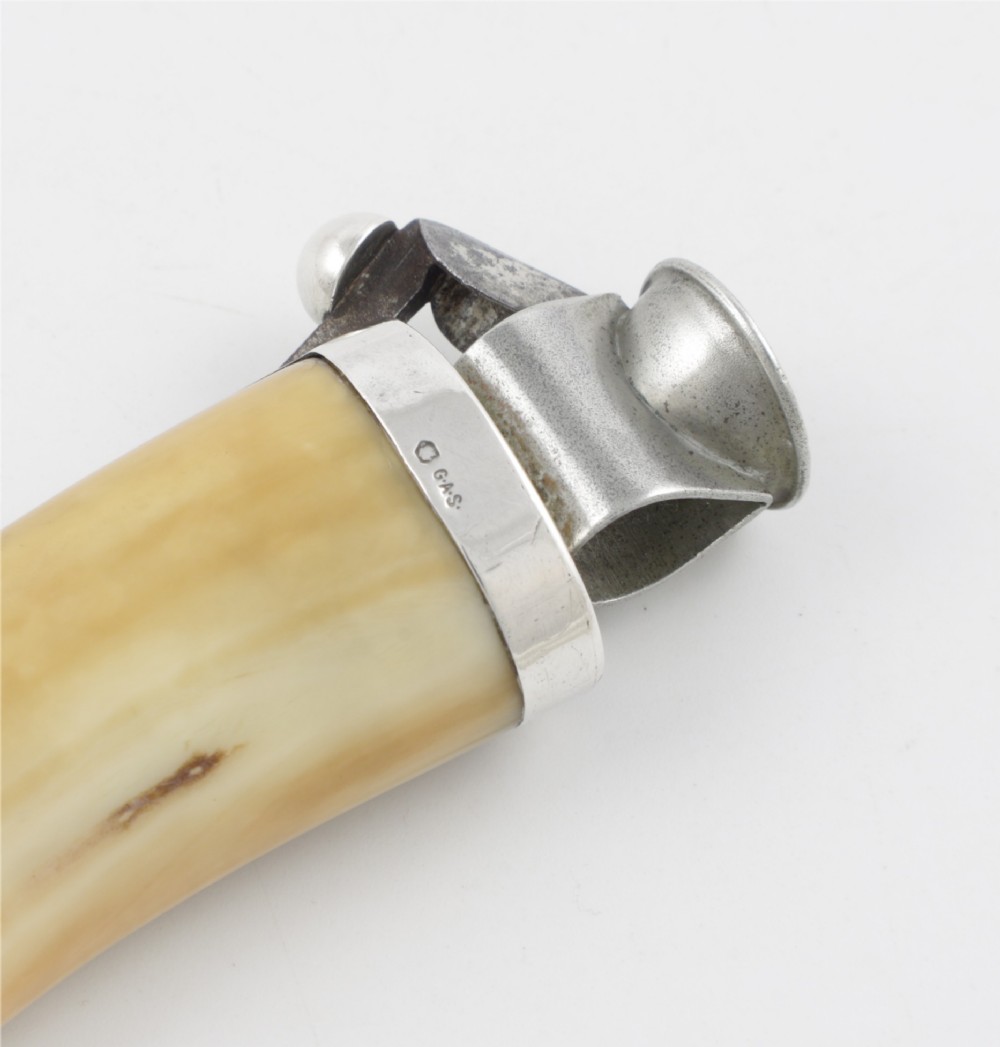 An antique cigar cutter crafted from a curved cream-coloured boar tusk fitted with a cast silver eagle head terminal and a silver cutting mechanism at the opposing end. View V