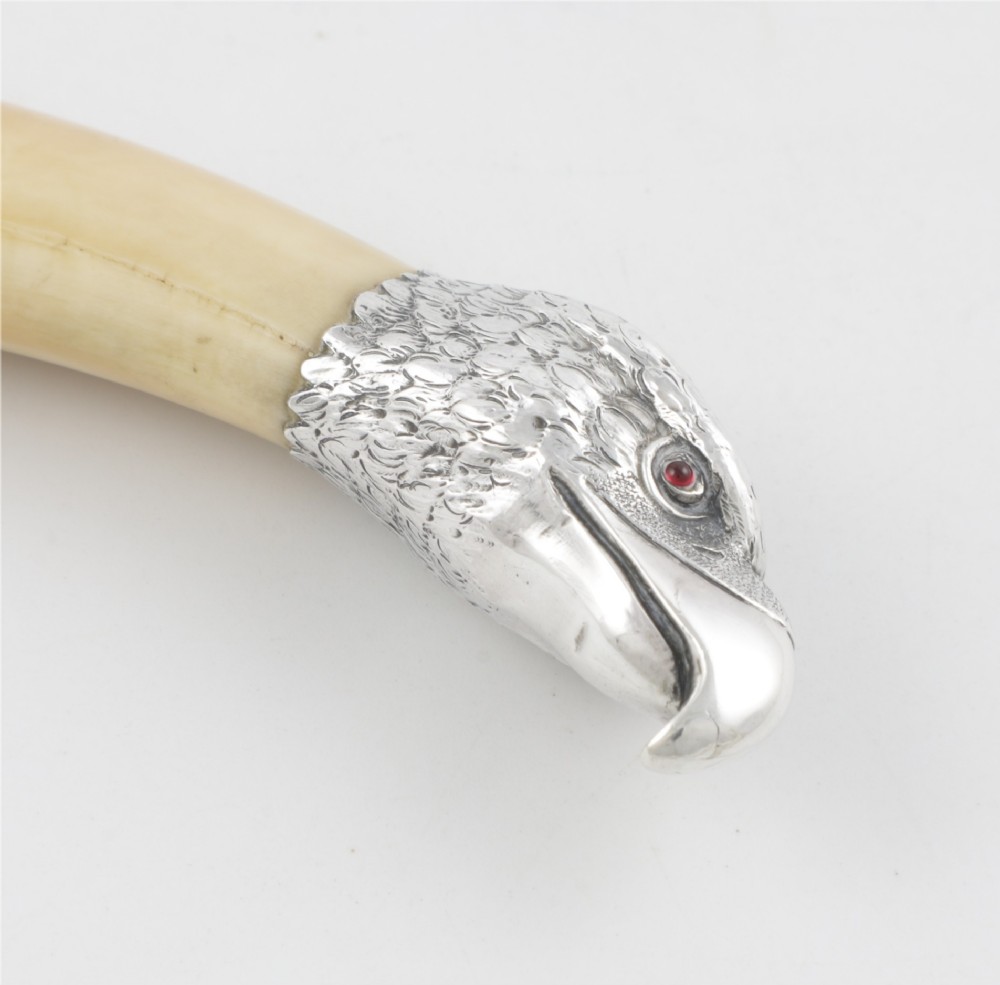 An antique cigar cutter crafted from a curved cream-coloured boar tusk fitted with a cast silver eagle head terminal and a silver cutting mechanism at the opposing end. View X