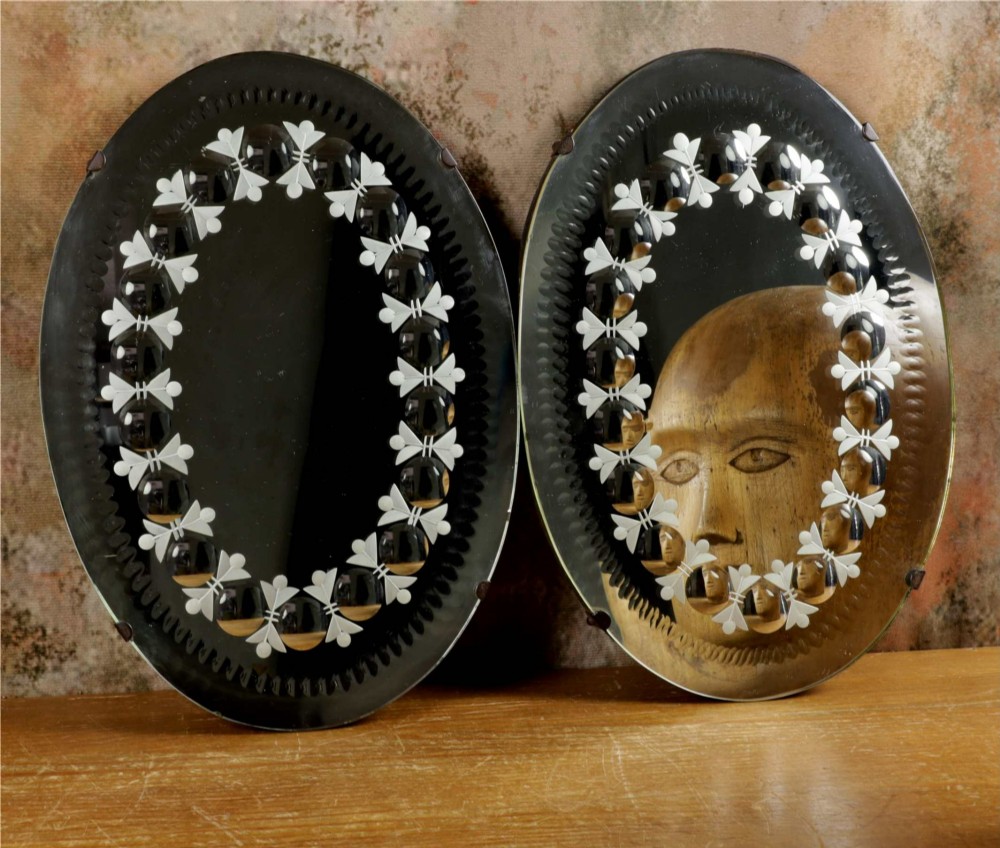 A pair of oval glass sorcerer mirrors featuring central dark reflections surrounded by a border of etched botanical motifs and raised convex glass lenses.