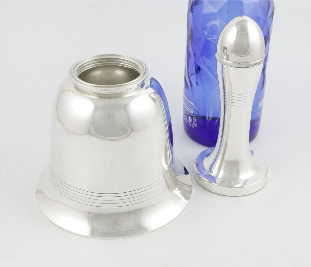 A silver plated novelty cocktail shaker in the shape of a handbell with a smooth turned handle and incised line detailing. View V