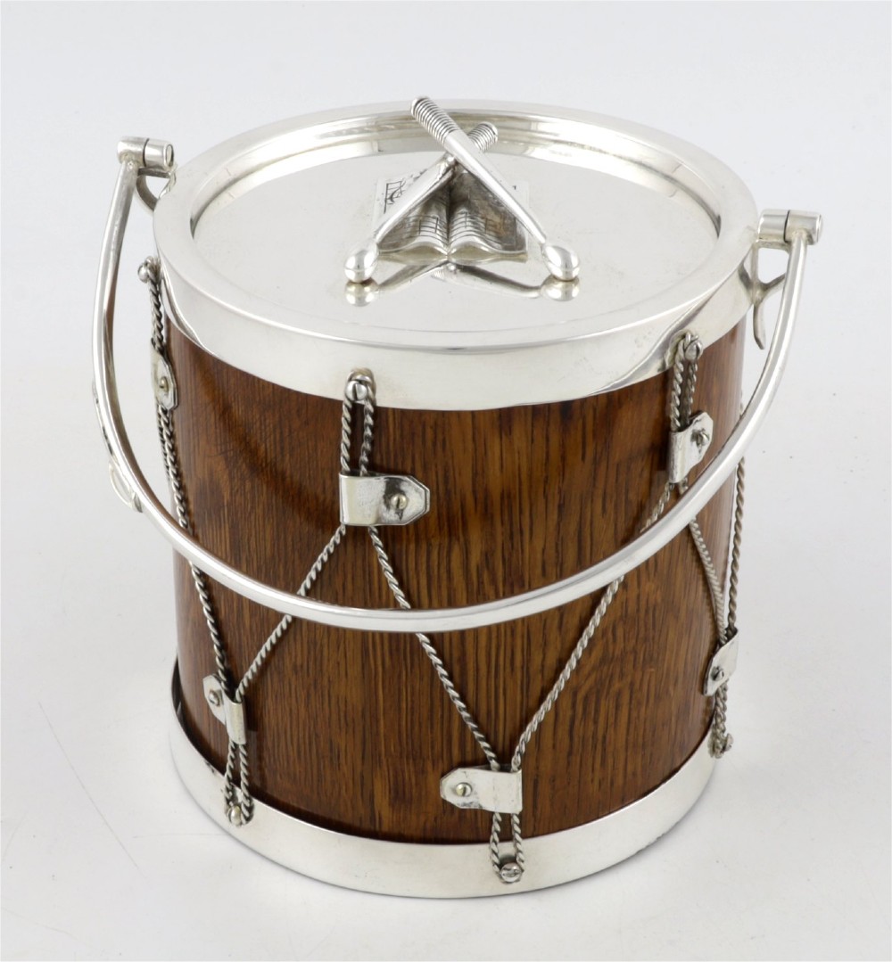 A cylindrical English oak ice pail shaped like a military drum, featuring silver-plated trim, rope-work detailing, a swing handle, and a lid topped with crossed drumsticks.