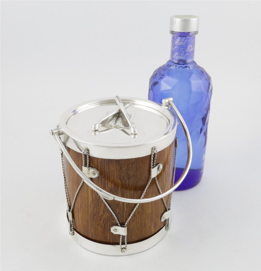 A cylindrical English oak ice pail shaped like a military drum, featuring silver-plated trim, rope-work detailing, a swing handle, and a lid topped with crossed drumsticks. View II