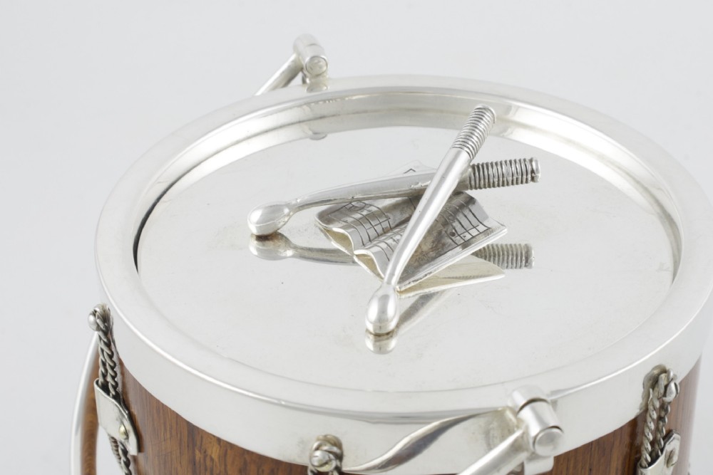 A cylindrical English oak ice pail shaped like a military drum, featuring silver-plated trim, rope-work detailing, a swing handle, and a lid topped with crossed drumsticks. View III