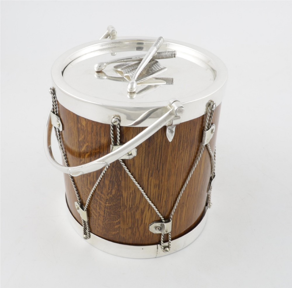 A cylindrical English oak ice pail shaped like a military drum, featuring silver-plated trim, rope-work detailing, a swing handle, and a lid topped with crossed drumsticks. View VIII