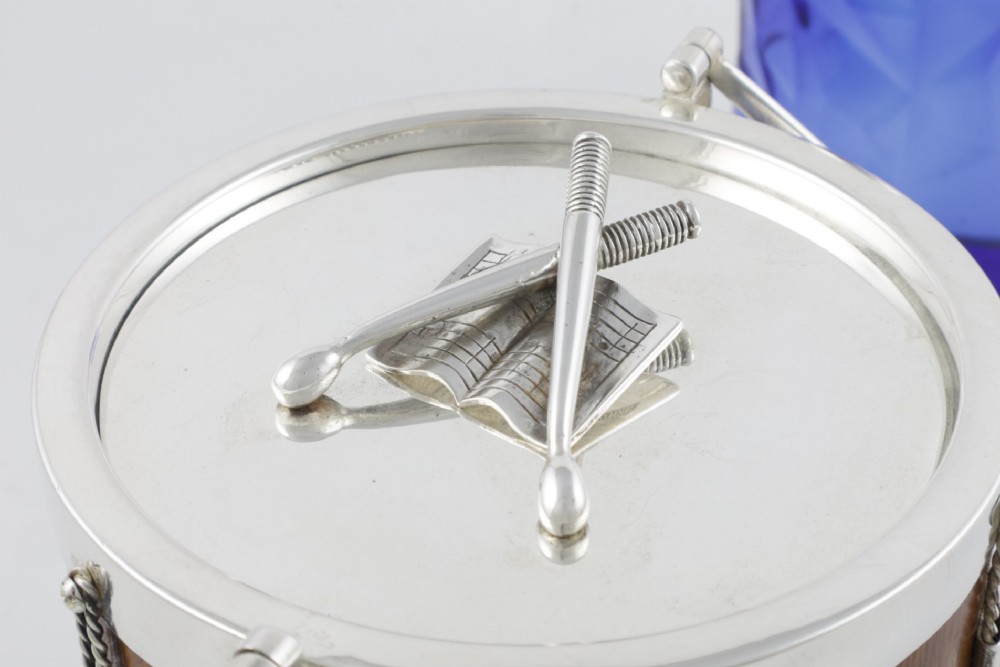 A cylindrical English oak ice pail shaped like a military drum, featuring silver-plated trim, rope-work detailing, a swing handle, and a lid topped with crossed drumsticks. View IX