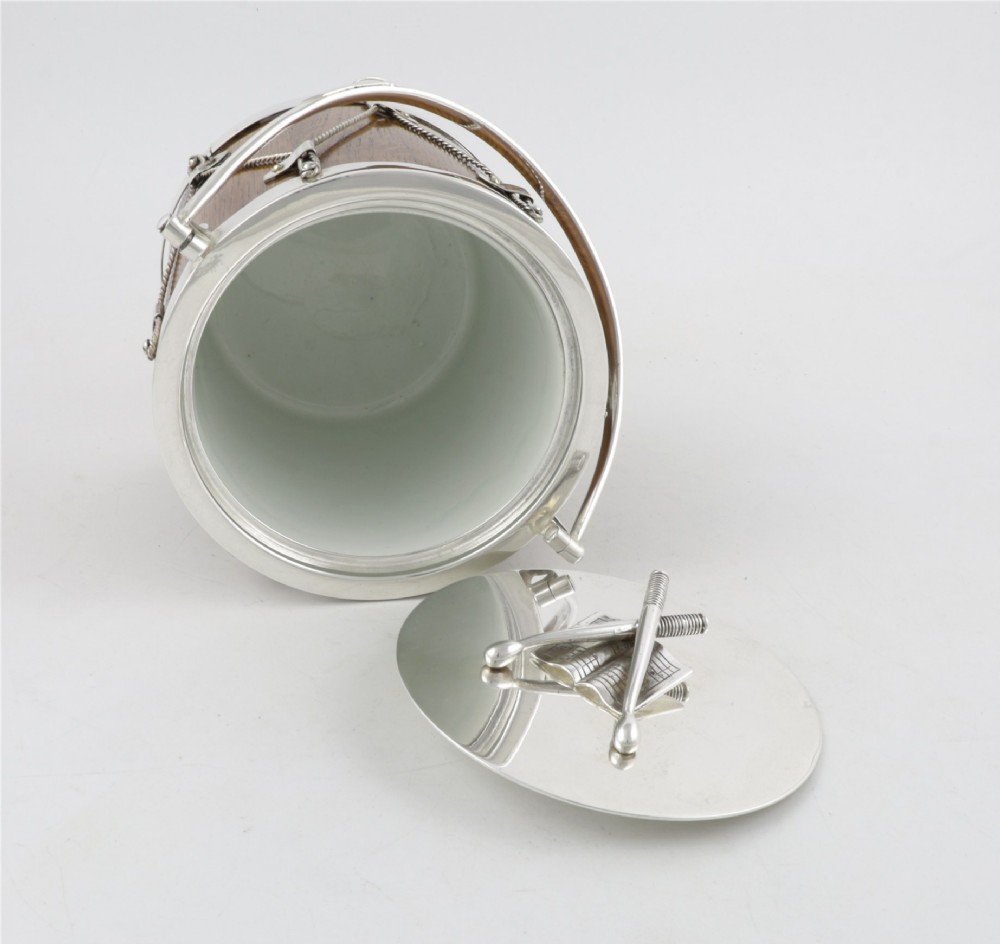 A cylindrical English oak ice pail shaped like a military drum, featuring silver-plated trim, rope-work detailing, a swing handle, and a lid topped with crossed drumsticks. View XI