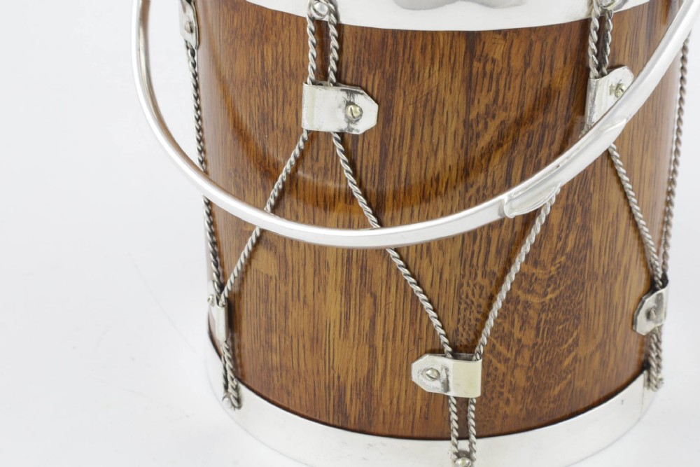A cylindrical English oak ice pail shaped like a military drum, featuring silver-plated trim, rope-work detailing, a swing handle, and a lid topped with crossed drumsticks. View XIII