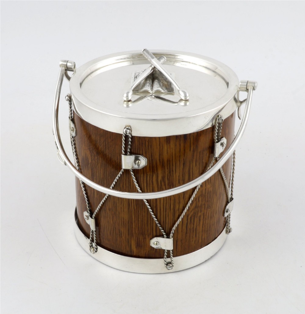 A cylindrical English oak ice pail shaped like a military drum, featuring silver-plated trim, rope-work detailing, a swing handle, and a lid topped with crossed drumsticks. View XIV