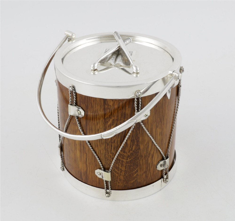 A cylindrical English oak ice pail shaped like a military drum, featuring silver-plated trim, rope-work detailing, a swing handle, and a lid topped with crossed drumsticks. View XV