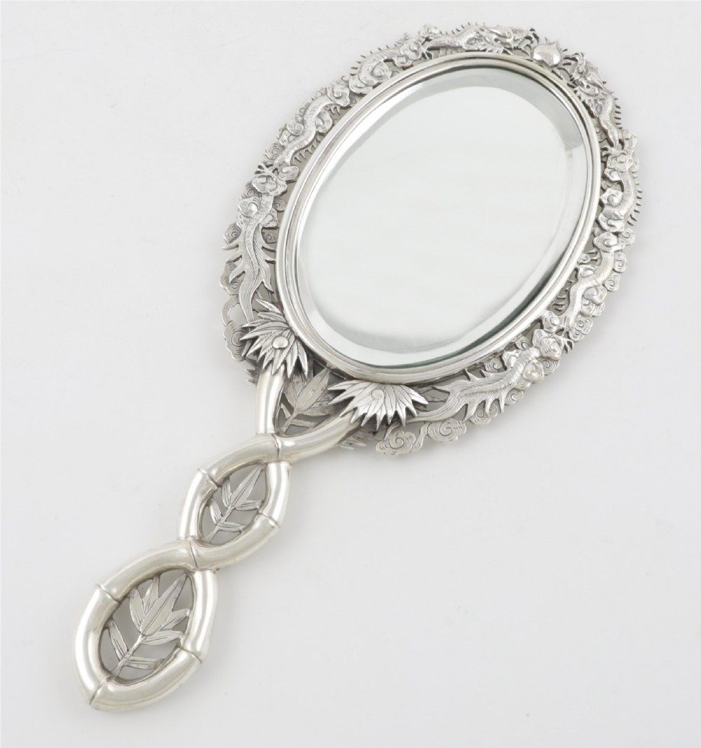 An antique silver hand mirror featuring a dragon motif frame and an interconnected faux-bamboo handle.