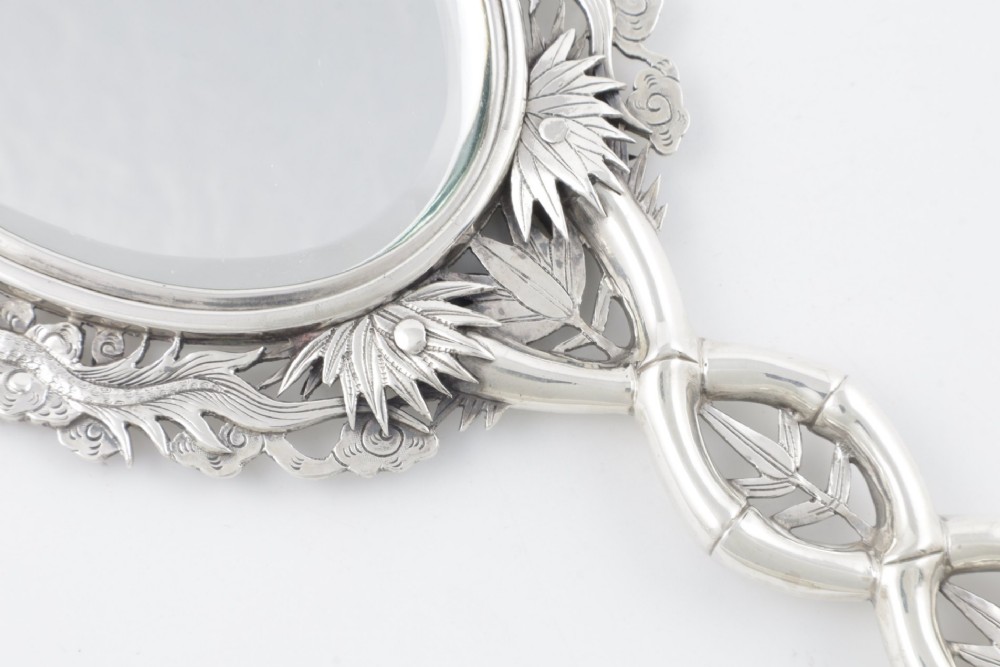 An antique silver hand mirror featuring a dragon motif frame and an interconnected faux-bamboo handle. View V