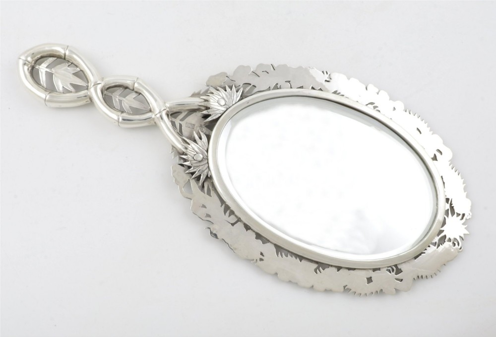 An antique silver hand mirror featuring a dragon motif frame and an interconnected faux-bamboo handle. View X