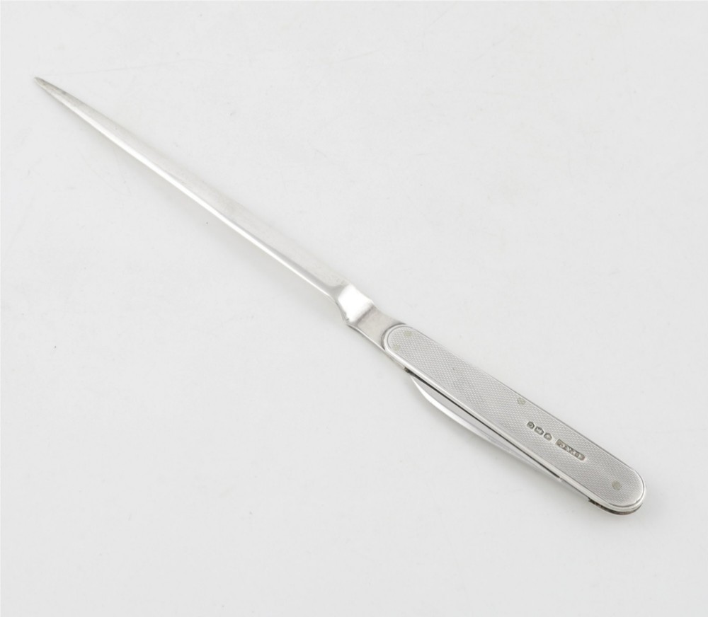 A vintage hallmarked sterling silver letter opener featuring an engine-turned handle casing with an integrated folding knife blade.