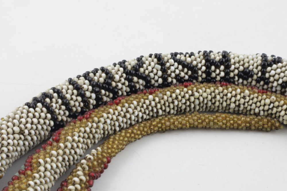 A long, hand-crafted glass beadwork snake with white, olive green, and red geometric patterns coiled into a spiral, featuring text reading TURKISH PRISONERS 1918 woven into its body. View III