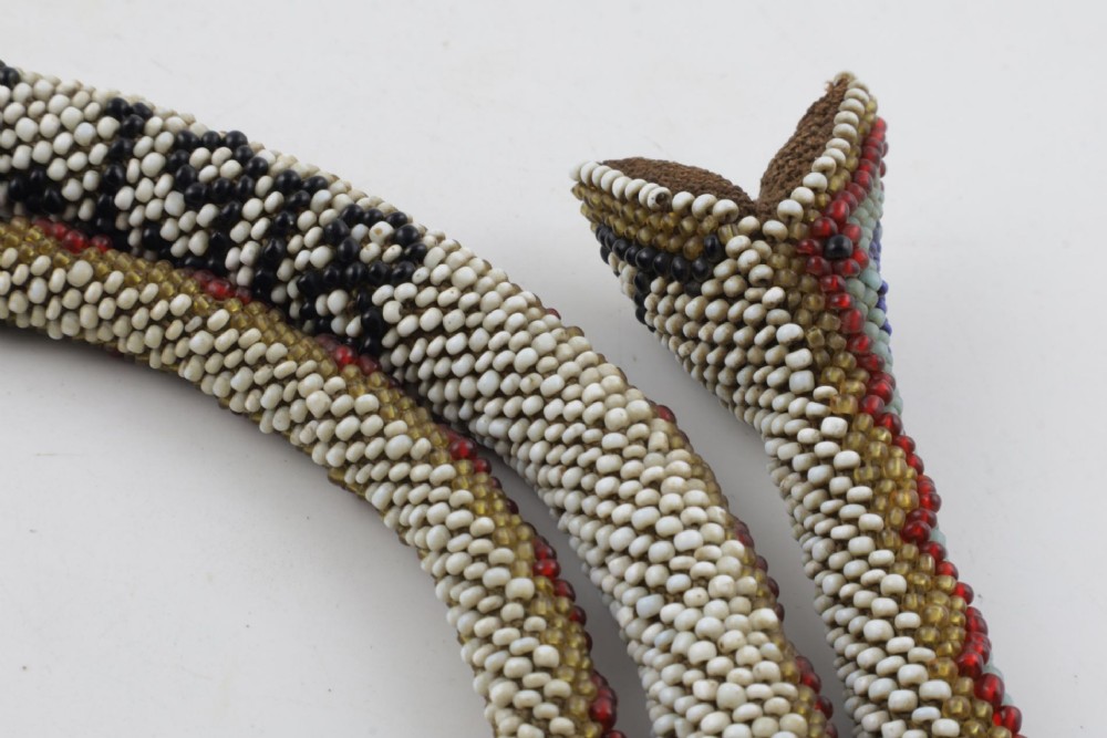 A long, hand-crafted glass beadwork snake with white, olive green, and red geometric patterns coiled into a spiral, featuring text reading TURKISH PRISONERS 1918 woven into its body. View V